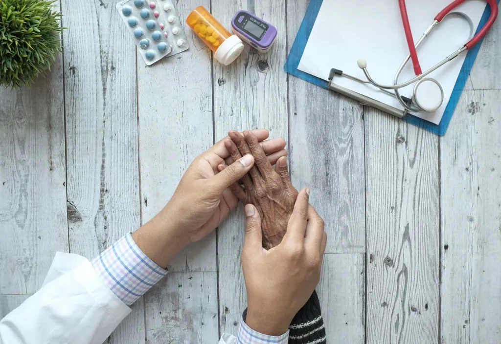 Médico segurando as mãos de paciente idoso em consulta
